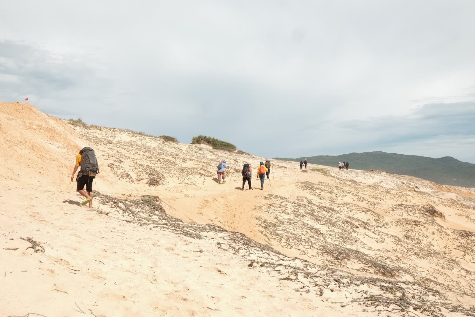 Đoàn đi bộ trên đồi cát, phía xa là biển.