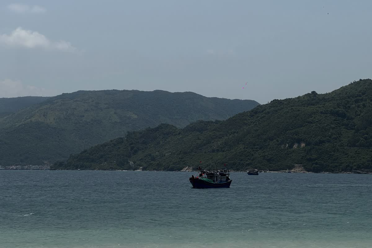 Thuyền đánh cá trên mặt biển, phía sau là núi.
