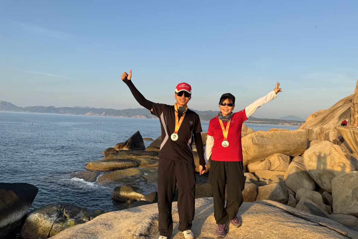 Hai người đeo huy chương giơ tay trên ghềnh đá ven biển.