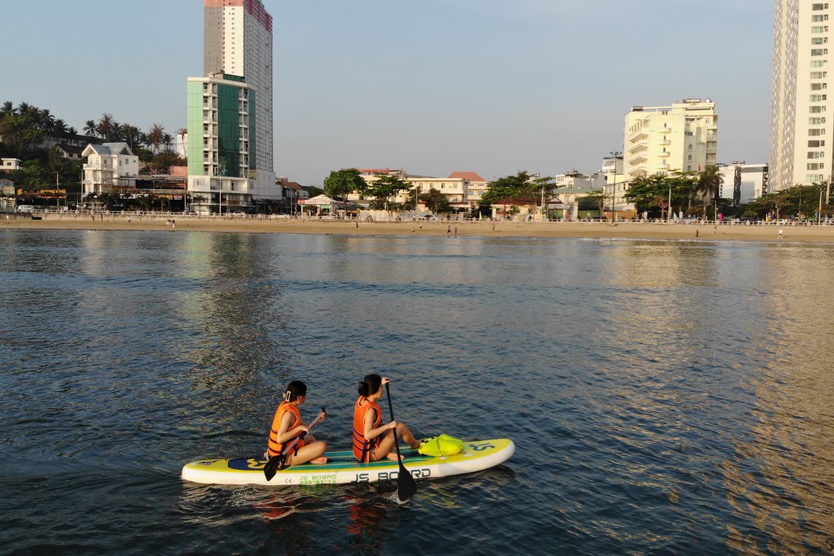 Hai người chèo SUP gần bờ, phía sau là thành phố.