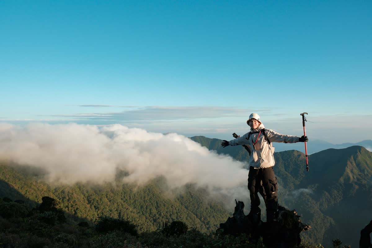 Giơ gậy trekking trên mỏm đá, phía sau là mây và núi.