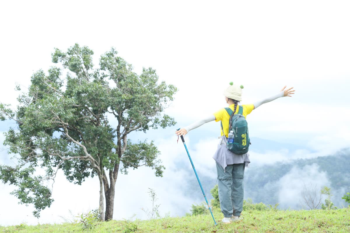 Dang tay trên đồi cỏ, thung lũng phía sau phủ mây.